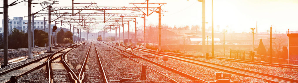 Railroad tracks stretching into the distance with a bright yellow train approaching in the background.
