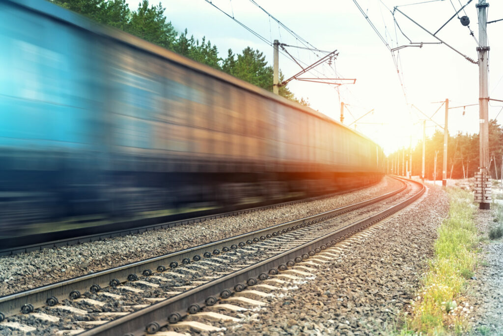 Motion blurred heavy cargo freight rusty train wagons moving on railway on sunset or sunrise day time. Industrial materials transportation and goods delivery concept. Old rusty wagons moving by rail