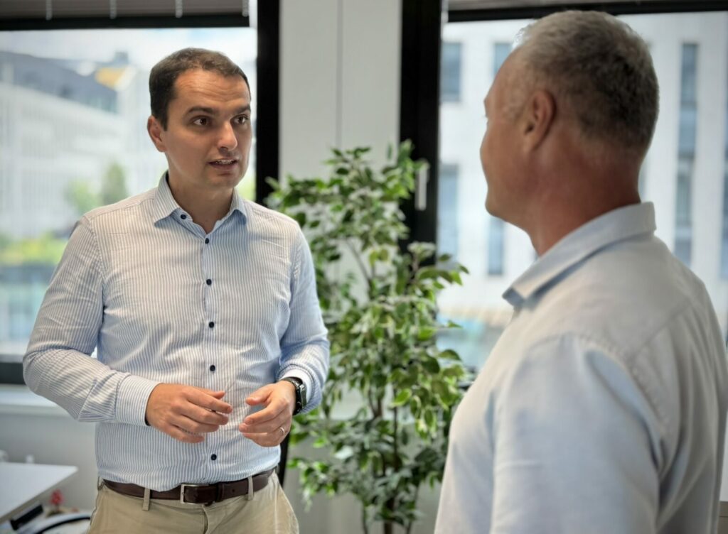 Andras Till portrait standing in the office talking with someone else
