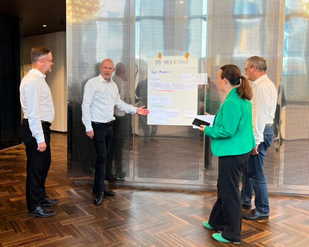 Management Board Meeting Sept 25 - Group Picture with Flipchart - Board Member Oliver Sellnick explaining Flip Chart about Members, other attendees listening.