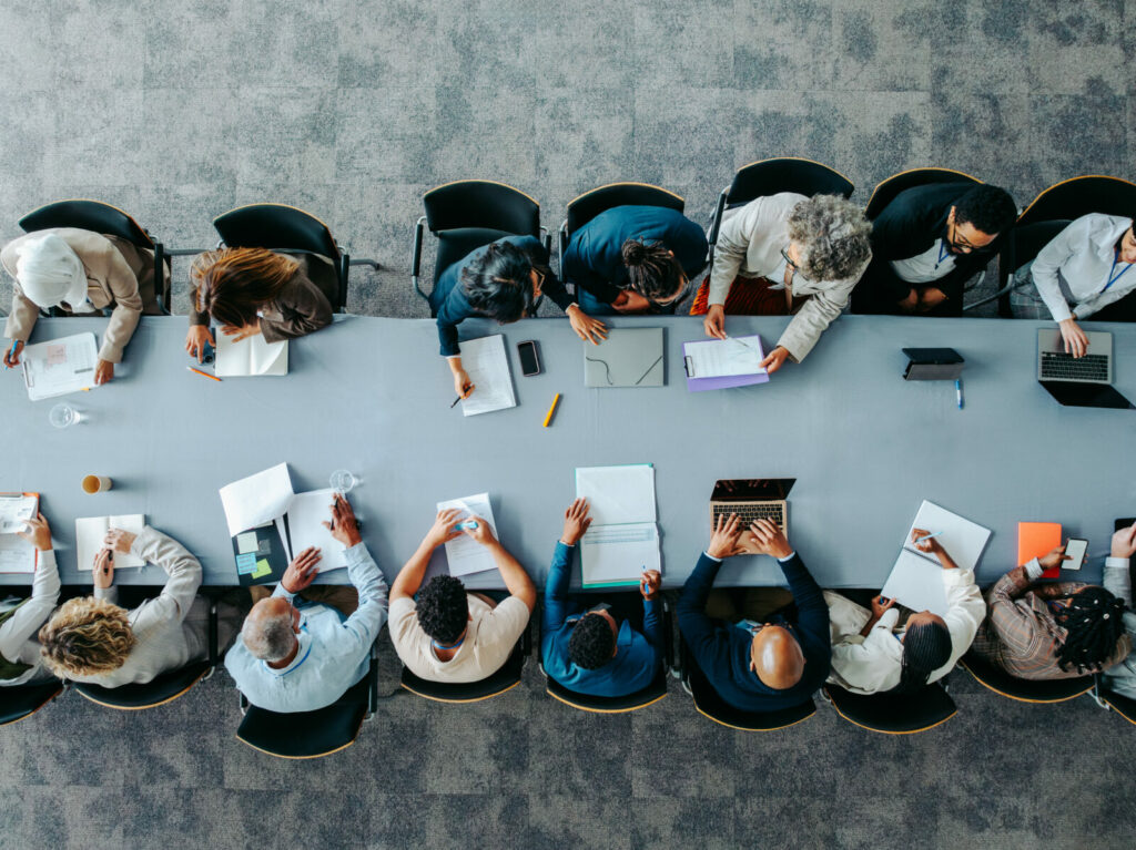 Overhead shot of business panel in office meeting collaborating around large table. Top view of diverse business group in office meeting, collaborating and discussing around a large table.